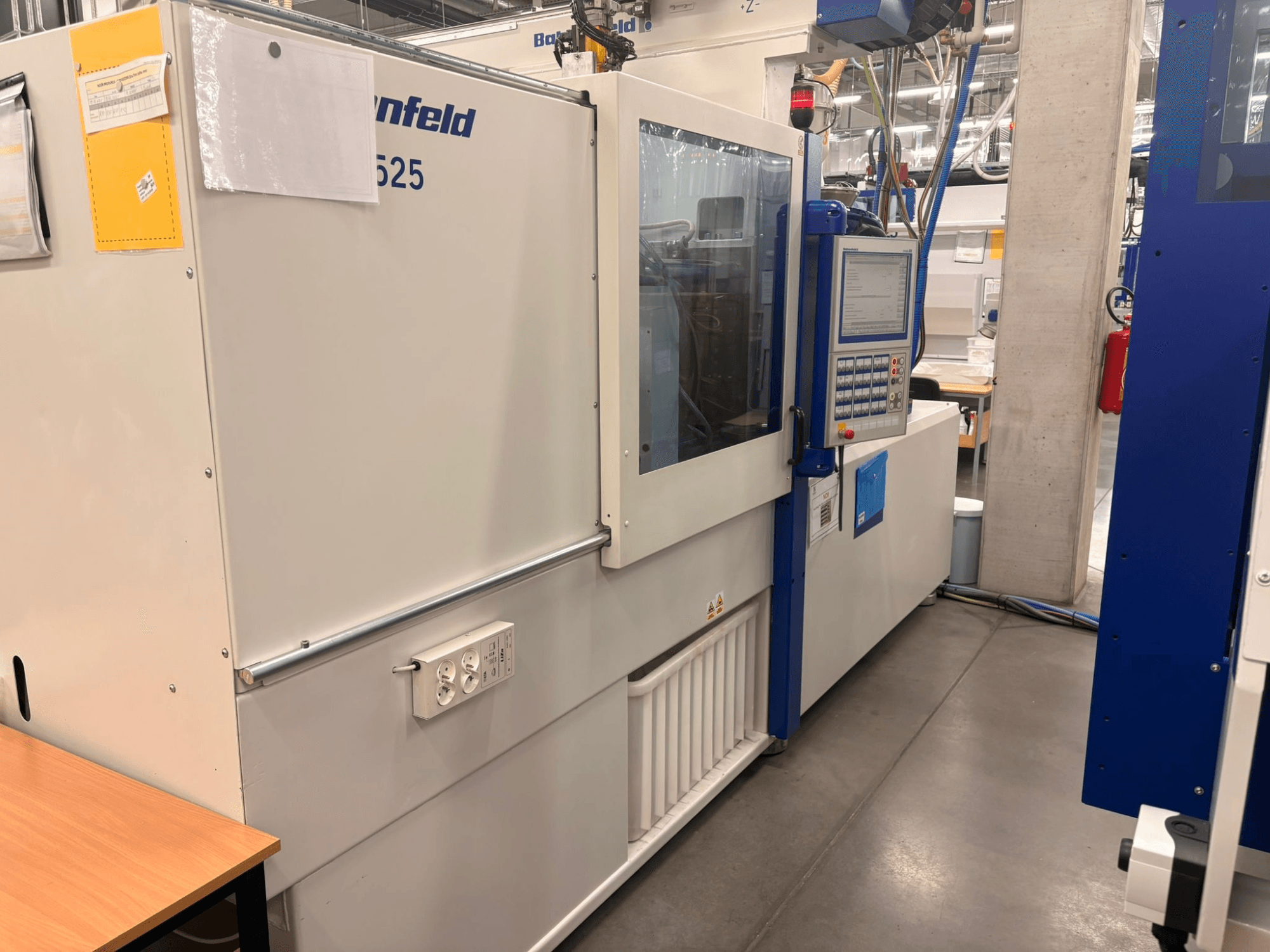 Machines by Arburg, model 620S, front view showcasing control panel and power ports in a factory setting.