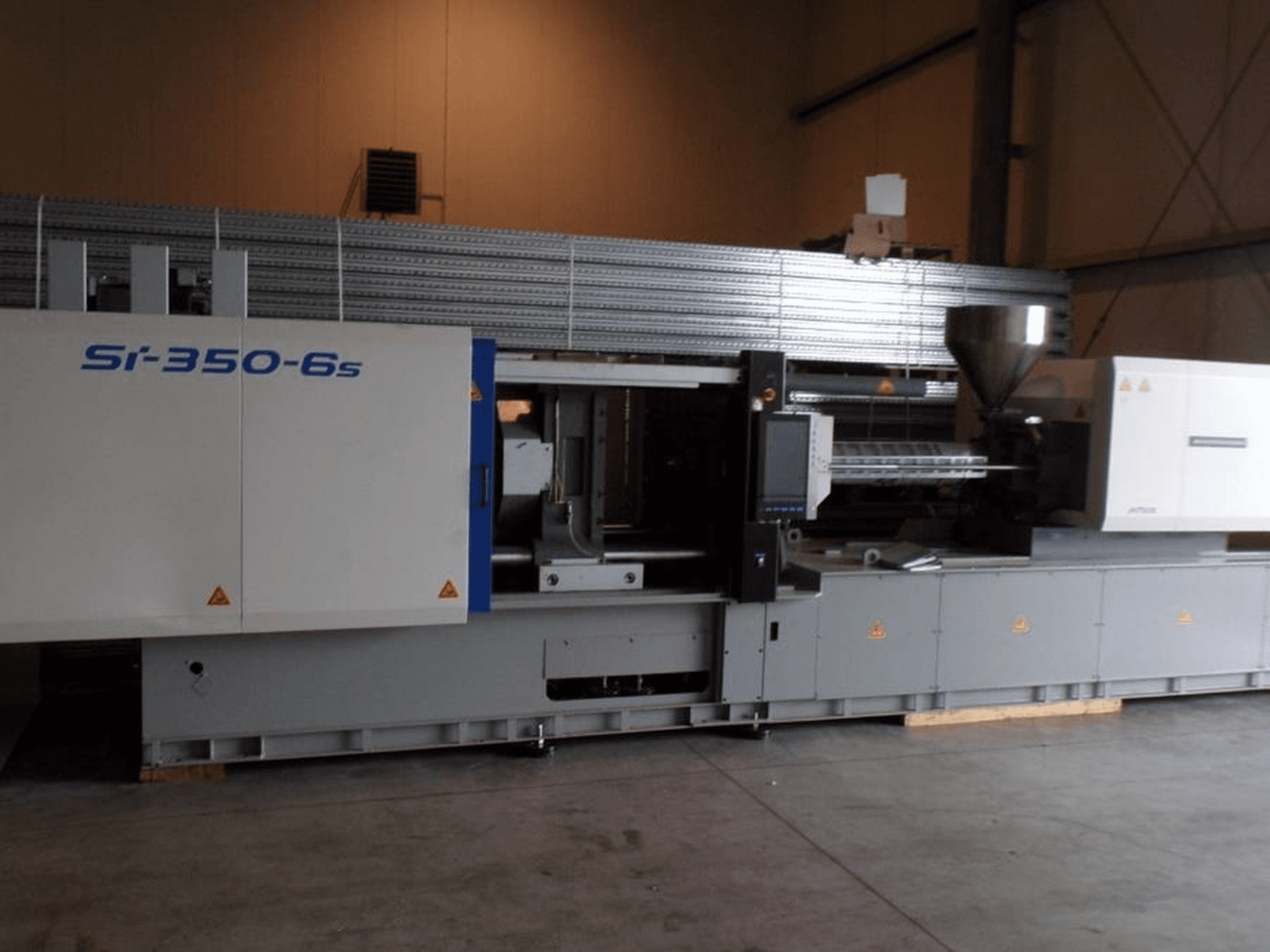Si-350-6s injection molding machine in side view, featuring a hopper and control panel, located in a spacious industrial setting.
