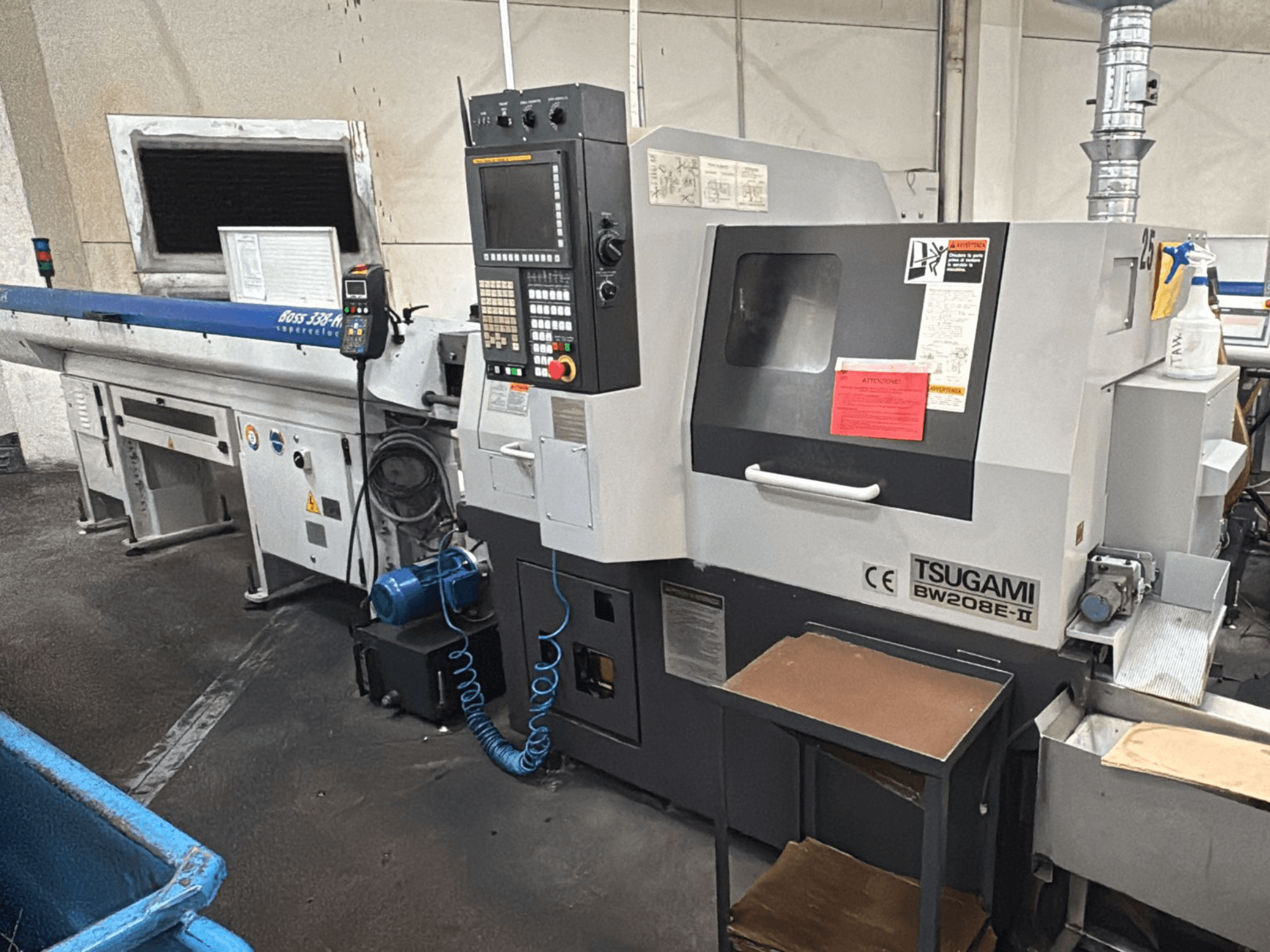 Tsugami BW208E-II CNC machine in a workshop, shown from a front angle, with control panel and safety labels visible.