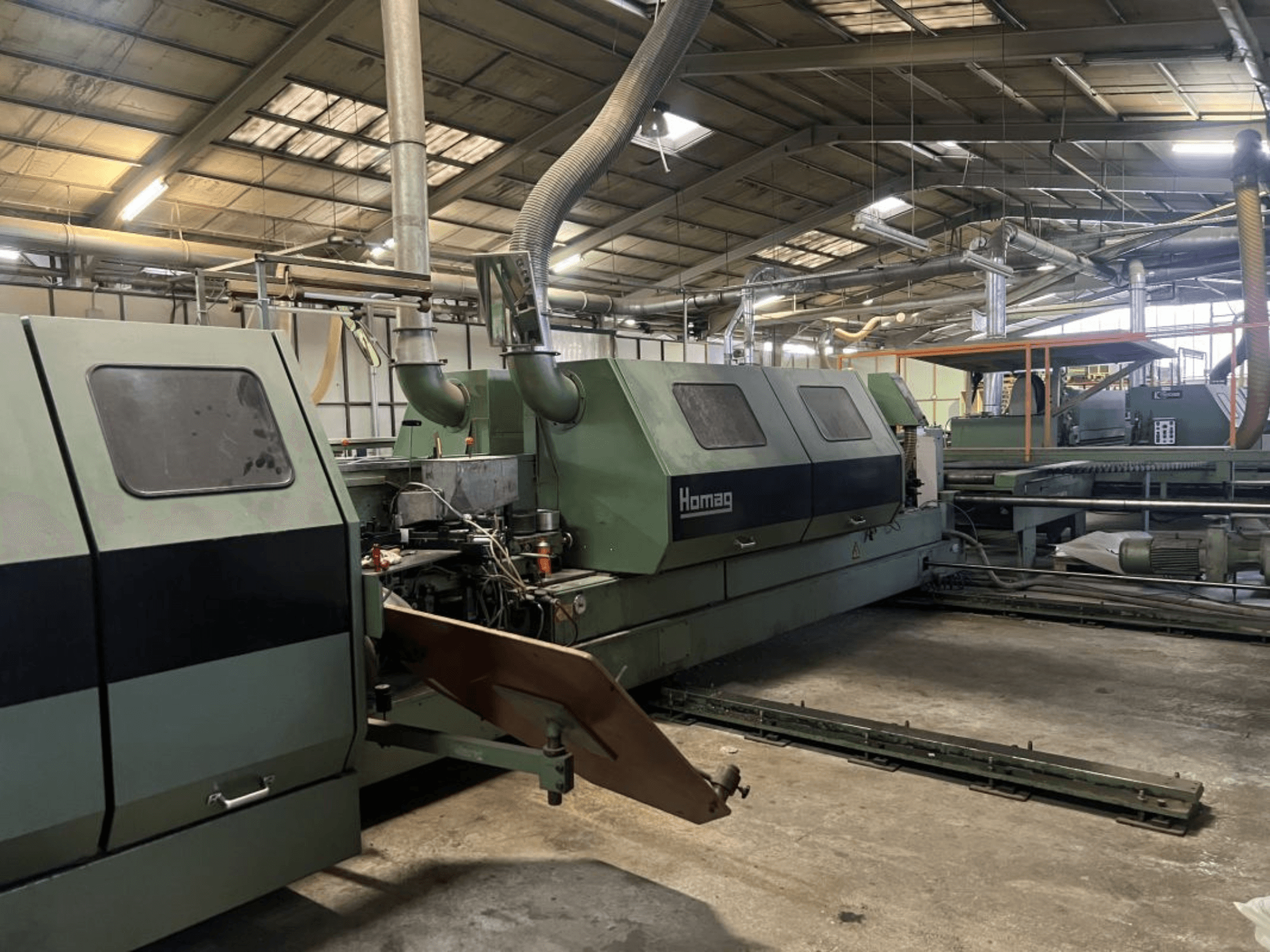 Homag industrial machine in green, side view, with operational components and control panel visible in a warehouse setting.