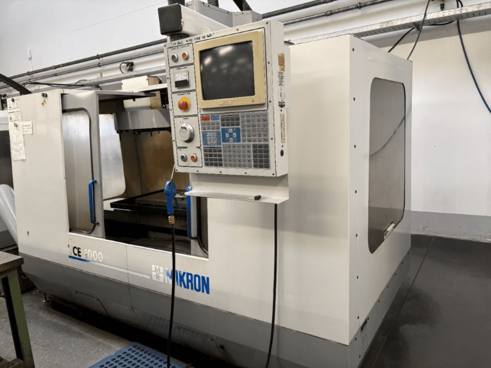 Mikron CE 2000 CNC machine, front view; features a control panel with buttons and screen, silver exterior, and working area.