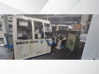 DECO 2000 machine viewed from the front, featuring control panel, pipes, and a cluttered workspace with tools and boxes.