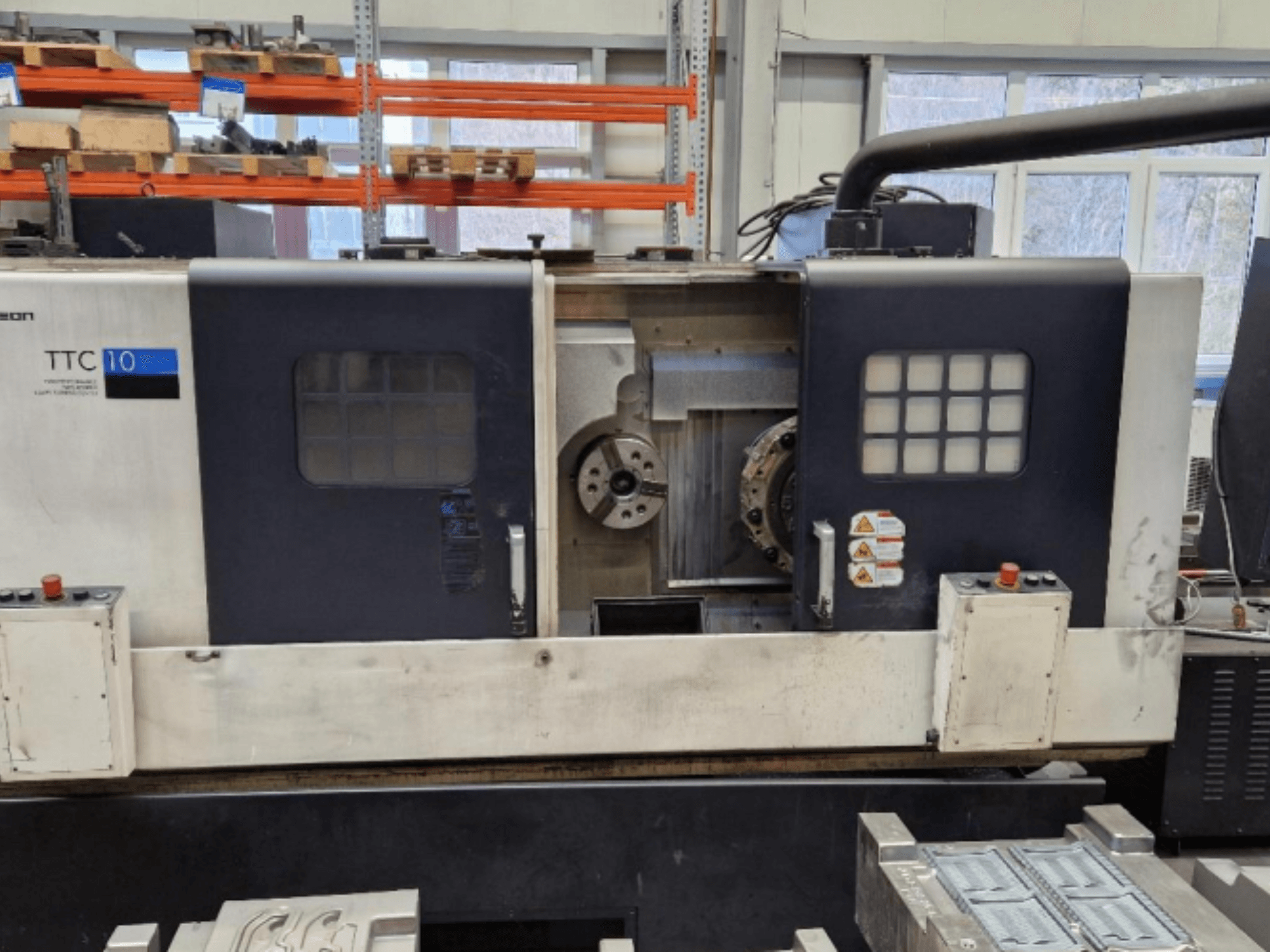TTC 10 lathe machine front view, showing control panel, visible chucks, and workspace with metal parts.