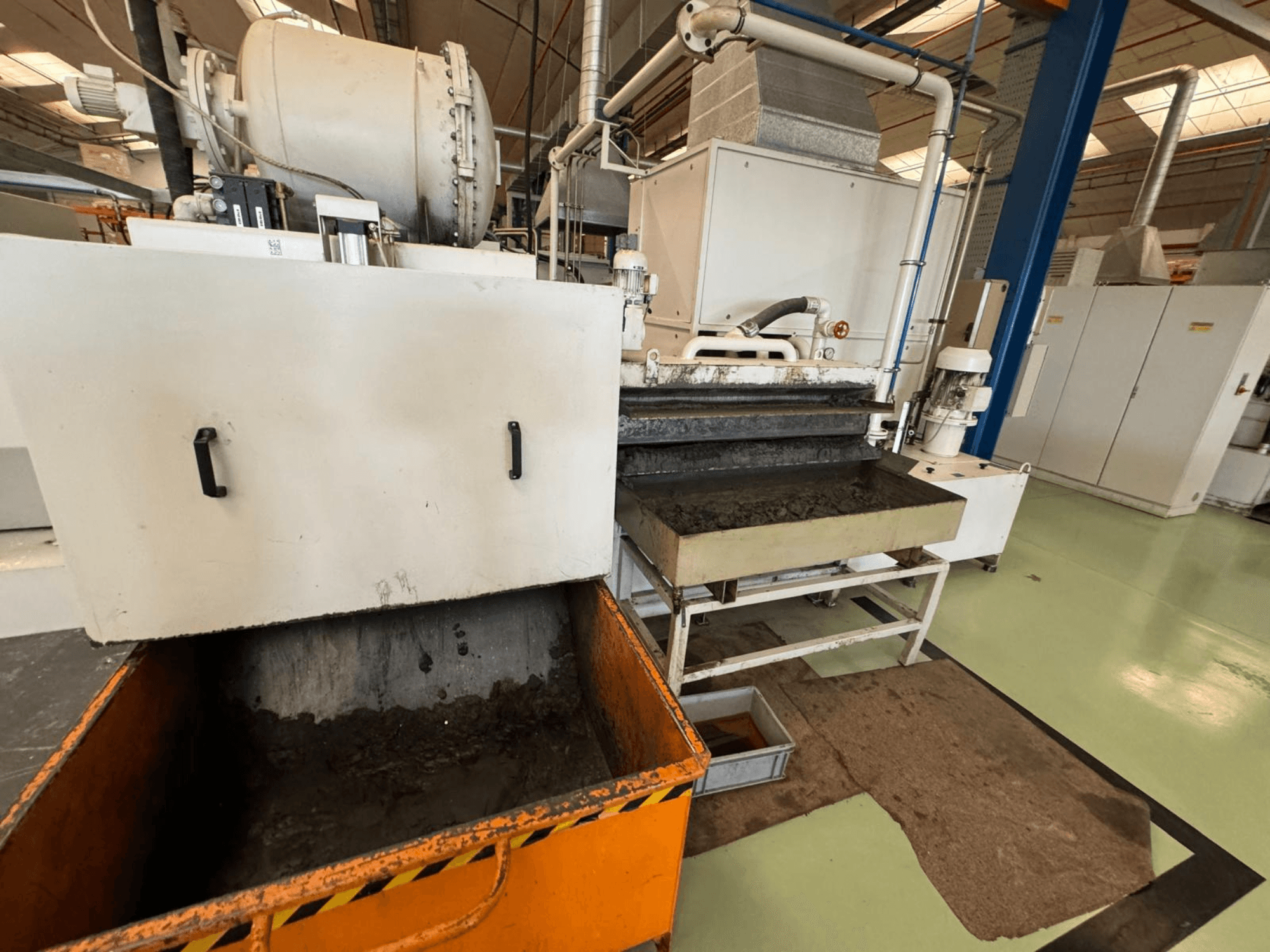 Industrial processing equipment with an orange waste bin, front view; contains a motor, conveyors, and maintenance area.