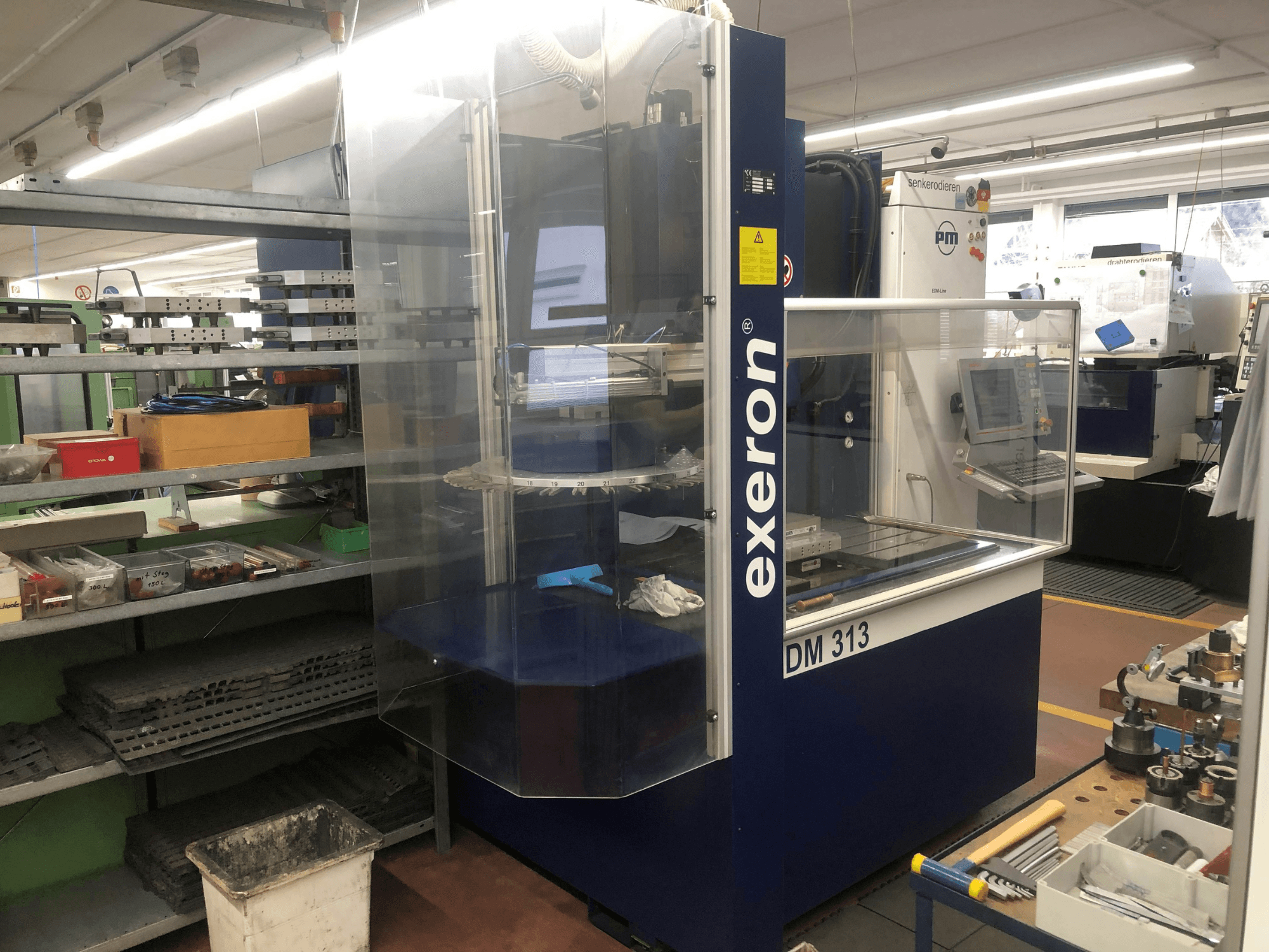 Exeron EDM 313 die-sinking machine in a workshop, showing front view with clear enclosure and control panel.