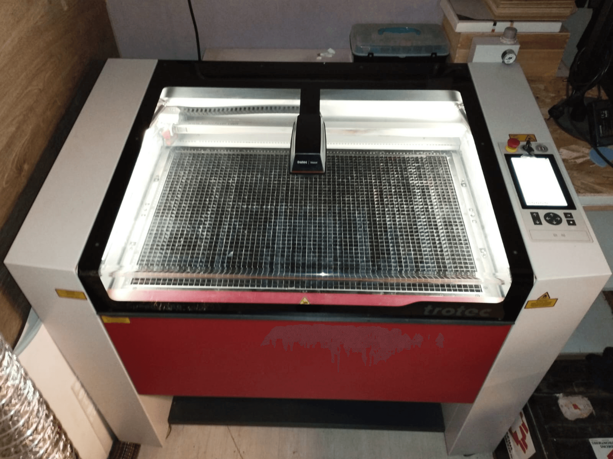 Trotec laser cutter with a transparent lid, grid bed, and control panel on the right; front view showcasing design and features.