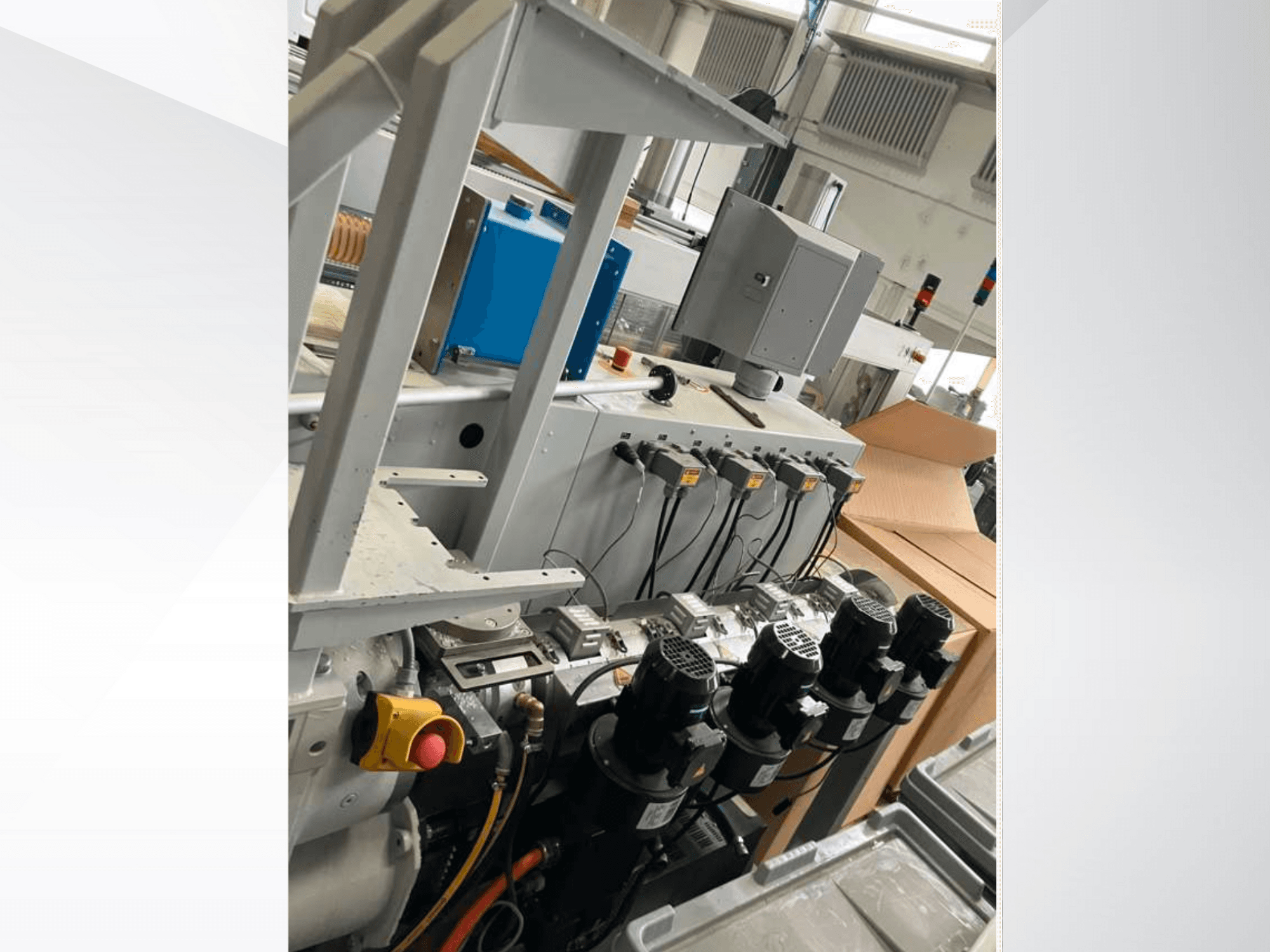 Industrial machinery control panel featuring multiple motors, gauges, and a monitor; side view inside a factory setting.