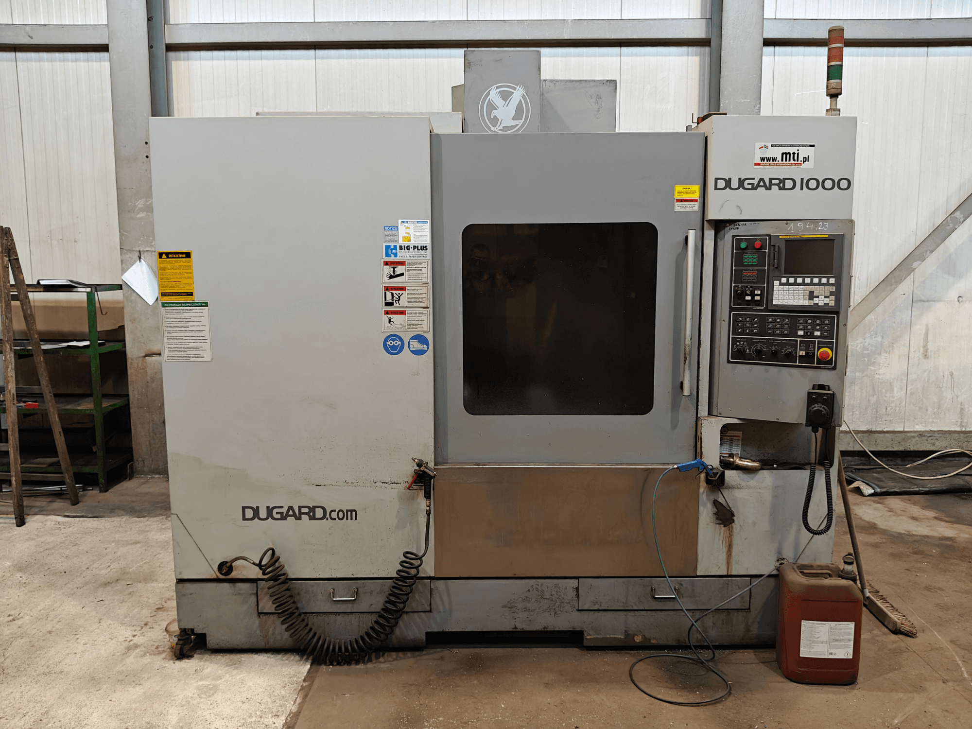 Dugard 1000 CNC machine, front view, showing control panel, safety labels, and oil container, in a workshop setting.