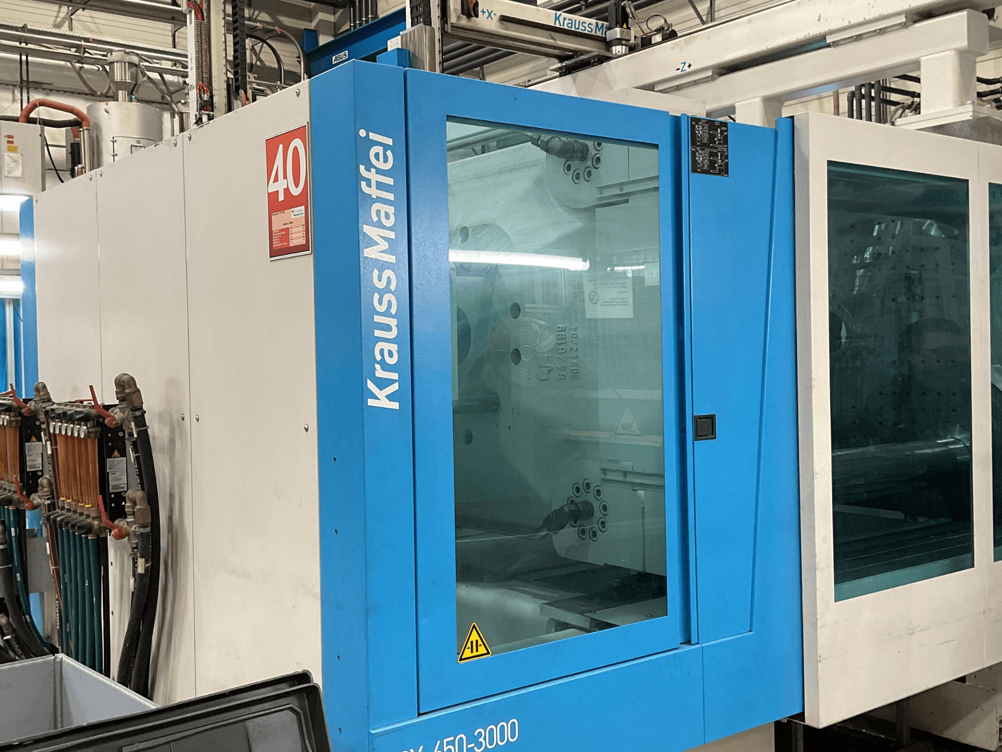 Krauss Maffei injection molding machine, model 450-3000, side view showing control panel and transparent safety door.