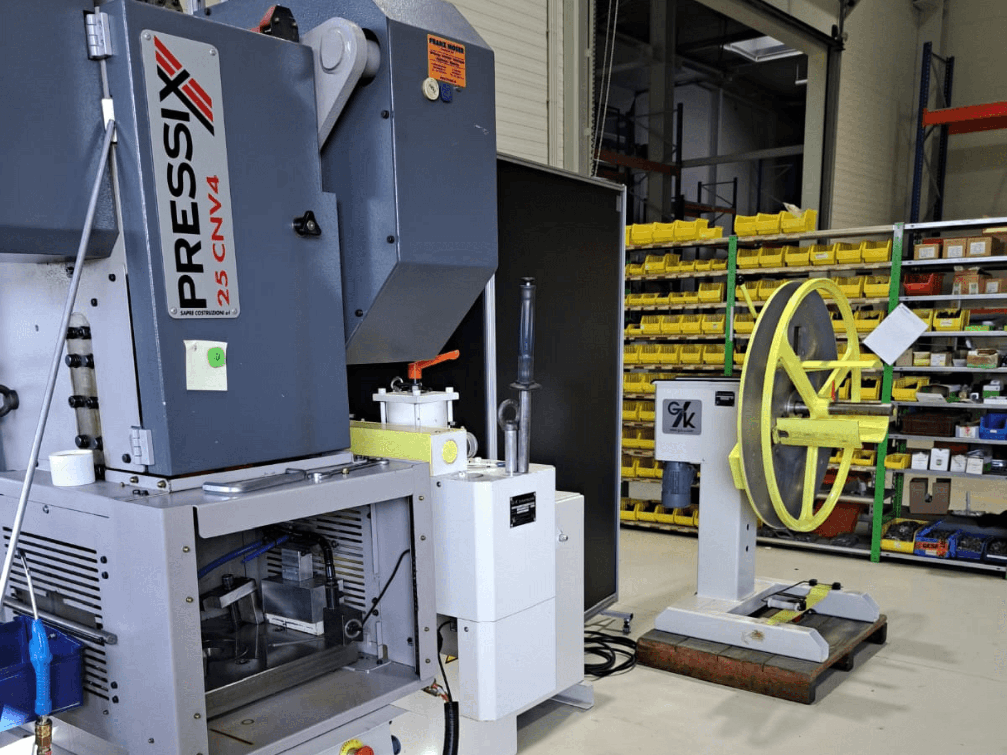 Industrial machine setup featuring PRESSIX 25 CNV4 on the left and a yellow wheel mounted on a gray base on the right, front view.