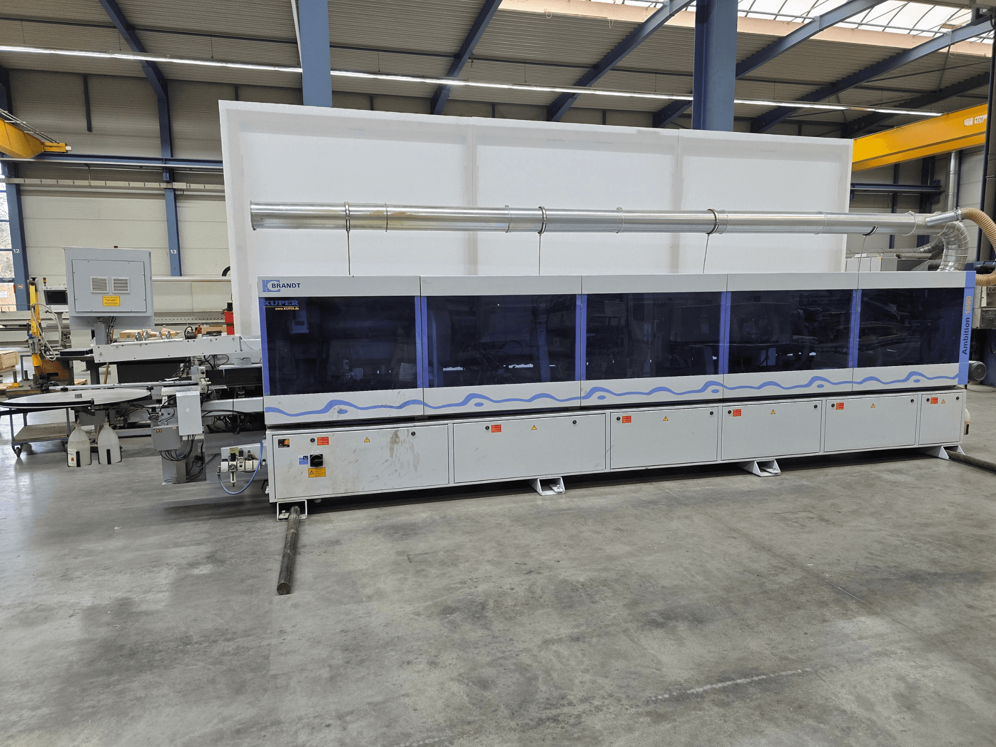Brandt KUPER machine in a factory, front view with transparent panels, featuring control buttons and safety warnings.