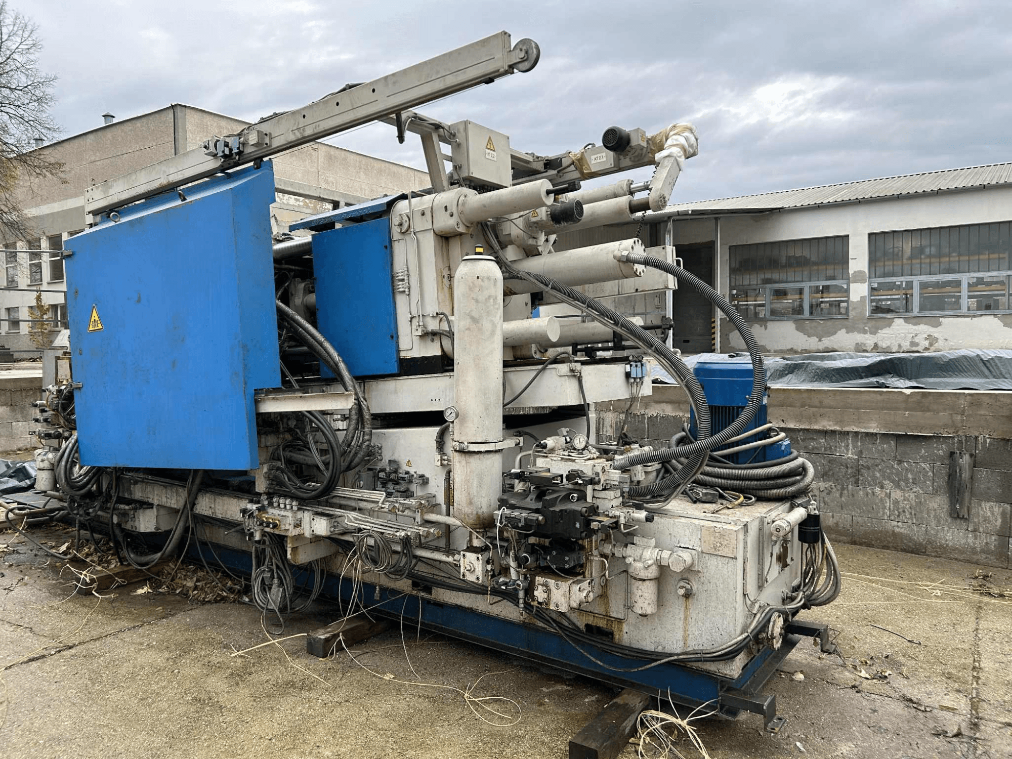 Large industrial hydraulic machine with blue casing, various hoses, and metal components, viewed from the side.