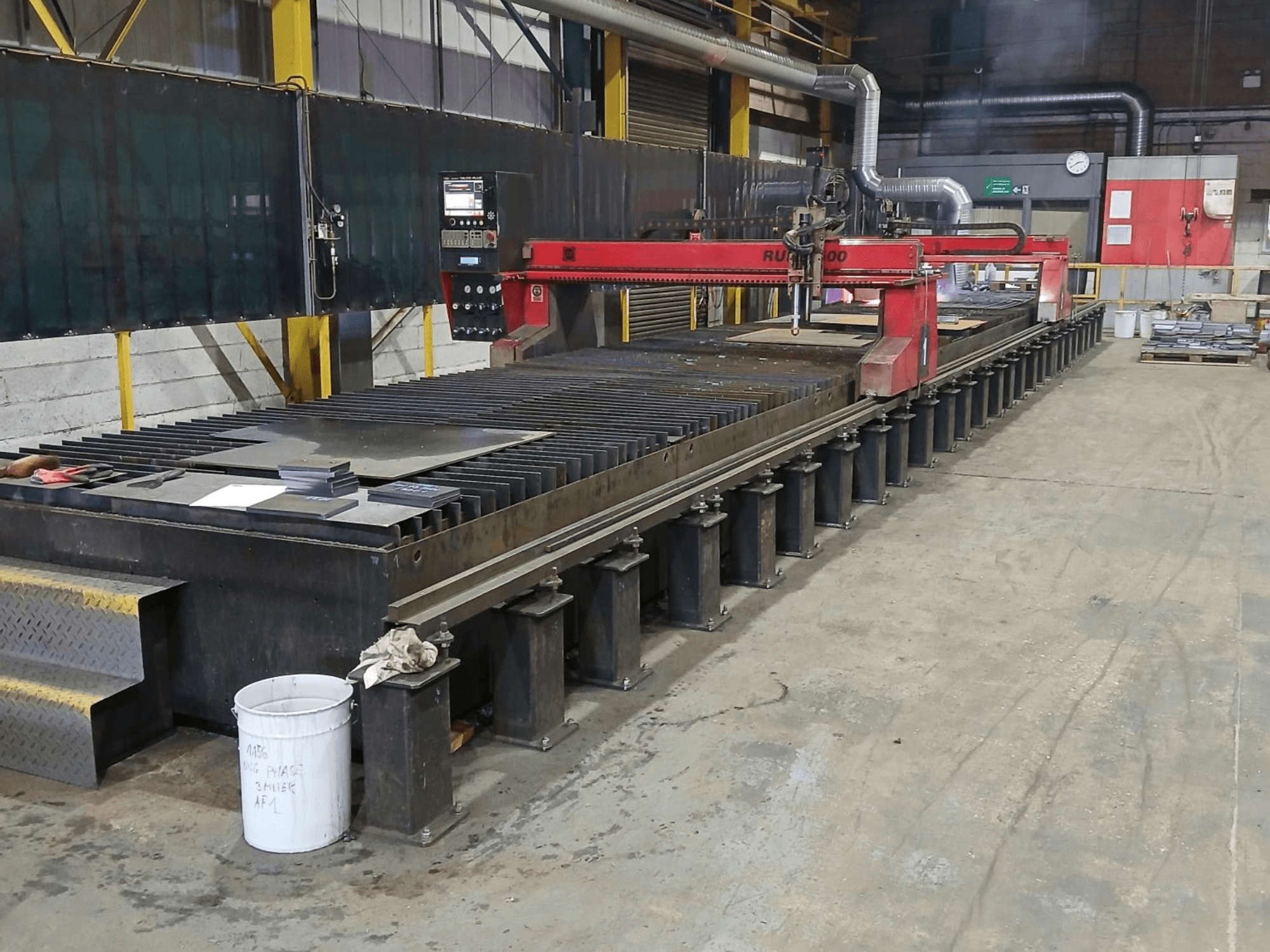 Red RUIDA 300 cutting machine, side view, with metal sheet on a steel table, located in an industrial workspace.