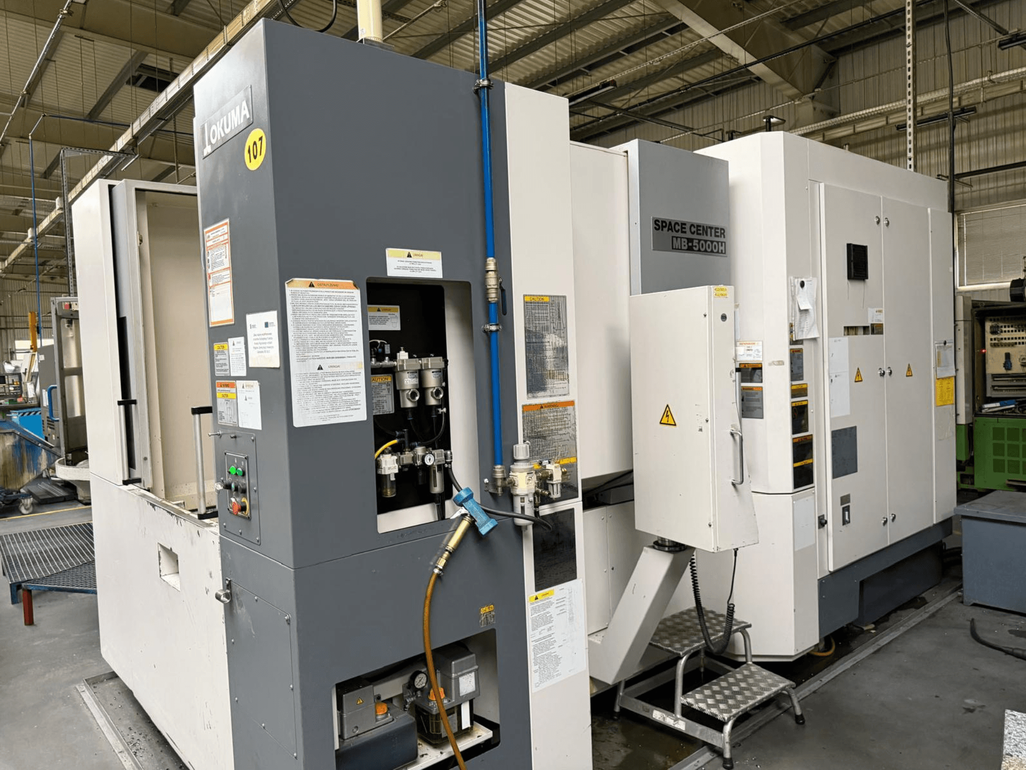 Okuma MB 5000H horizontal machining centre, side view showcasing control panel and machinery components in a factory setting.