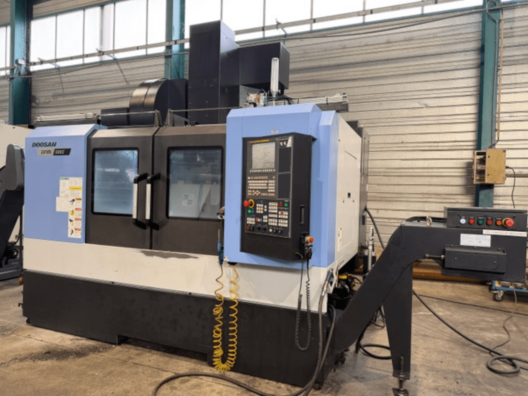Doosan DNM 500II CNC milling machine in front view, featuring control panel and tool holder, in a factory setting.
