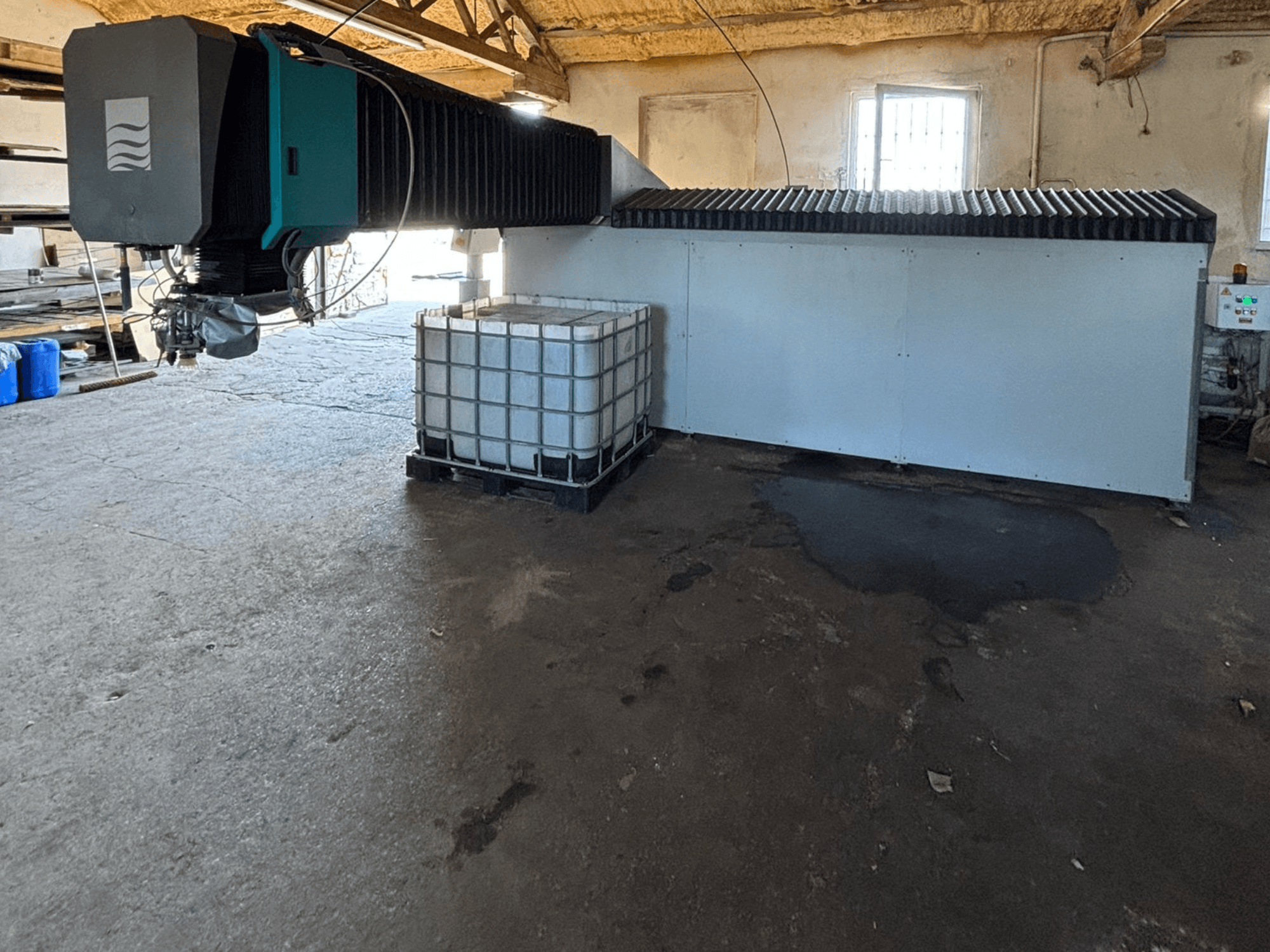 Industrial water jet machine in a workshop, side view, with a large water tank and control panel visible beside it.