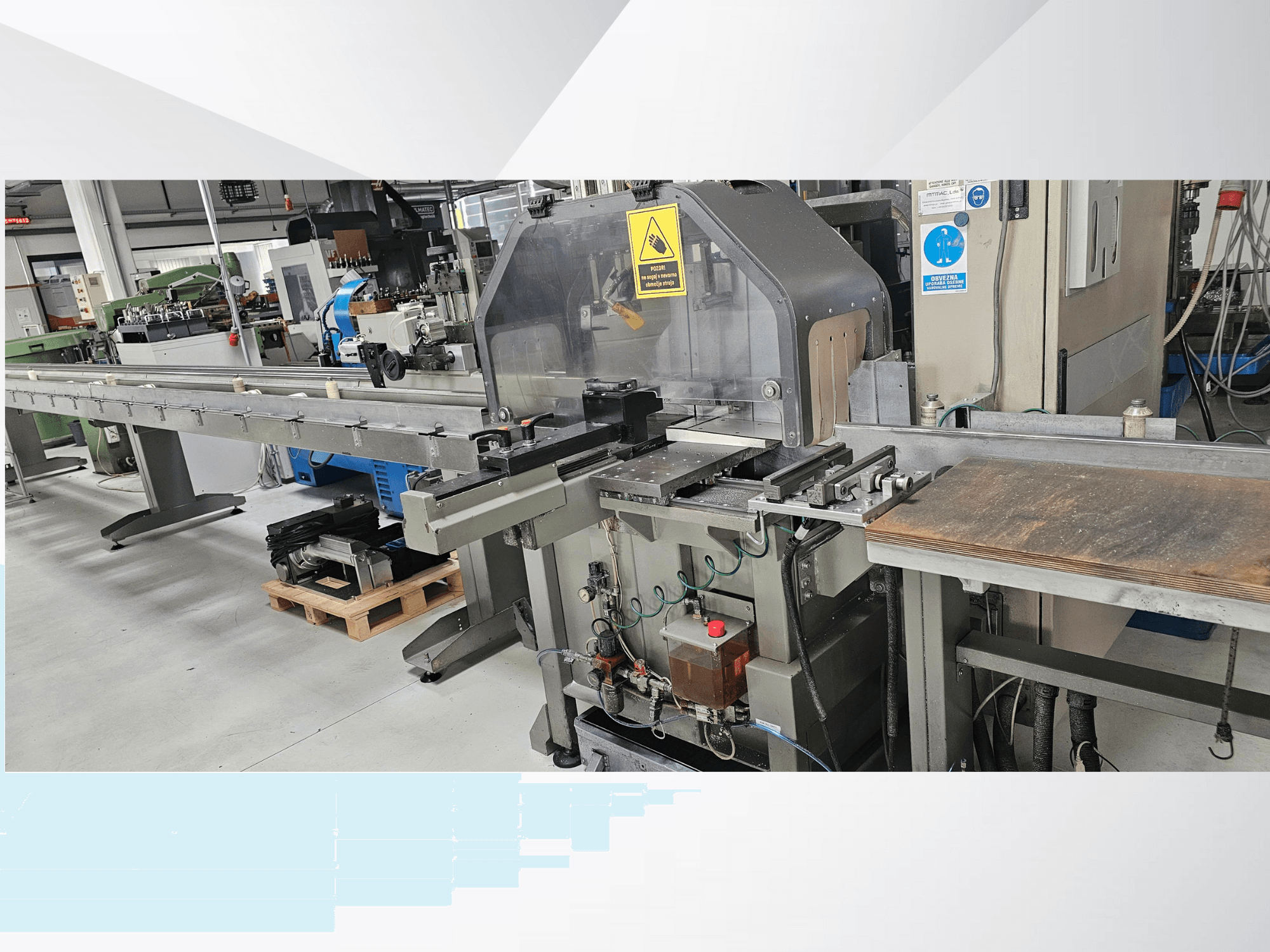 Industrial cutting machine from a side view, featuring a long conveyor, control panel, and safety warnings.
