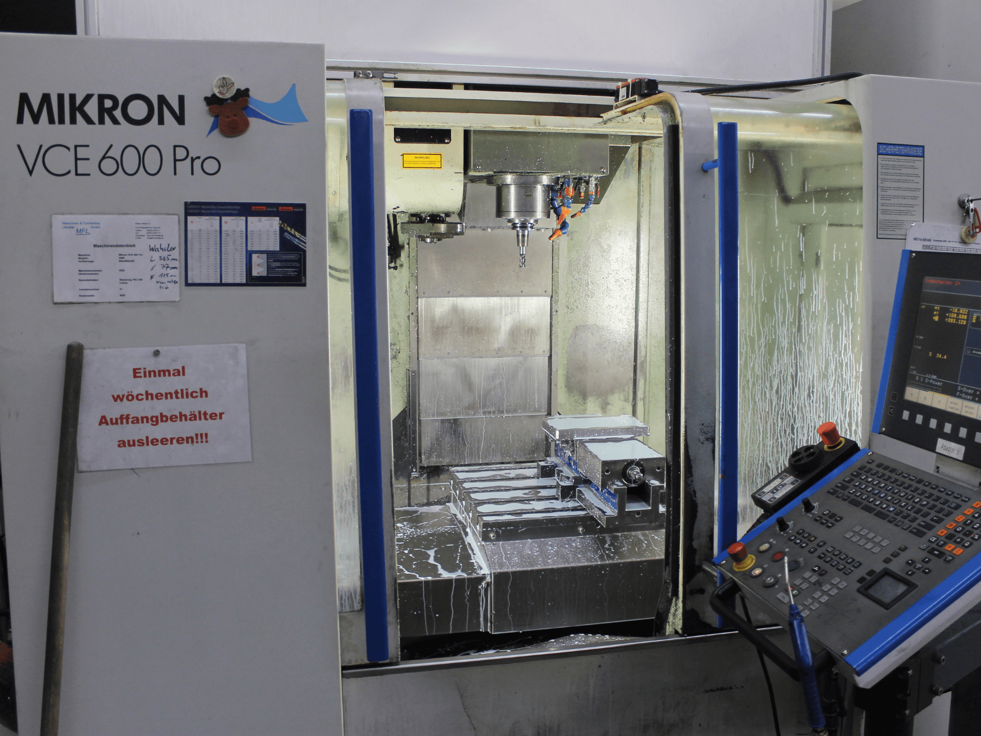 Mikron VCE 600 Pro machining center, front view, features cutting tools, coolant spray, and control panel with buttons.