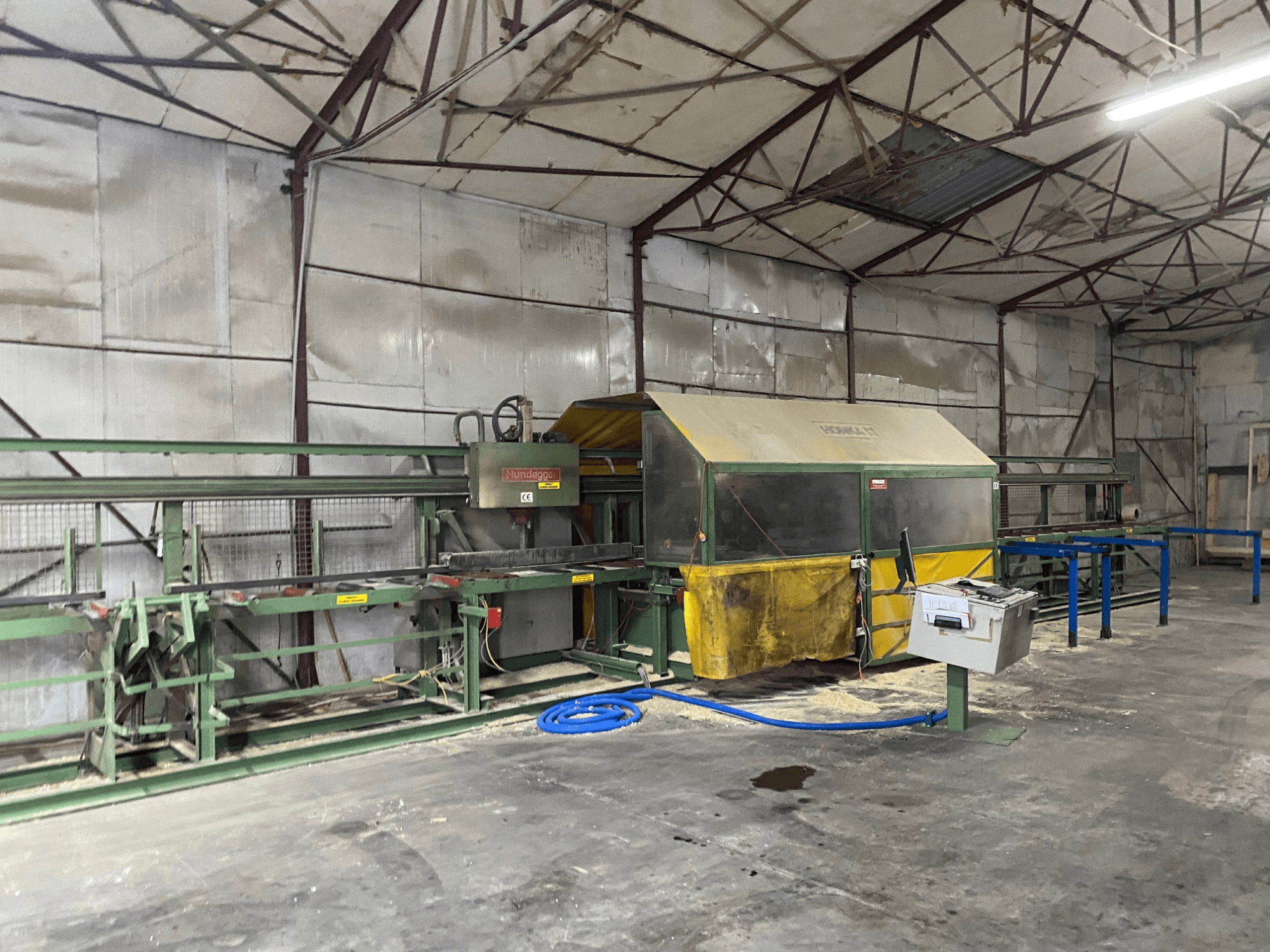CNC Wood Machining Centre HUNDEGGER K1 in a workshop, side view showing machinery, controls, and sawdust on the floor.
