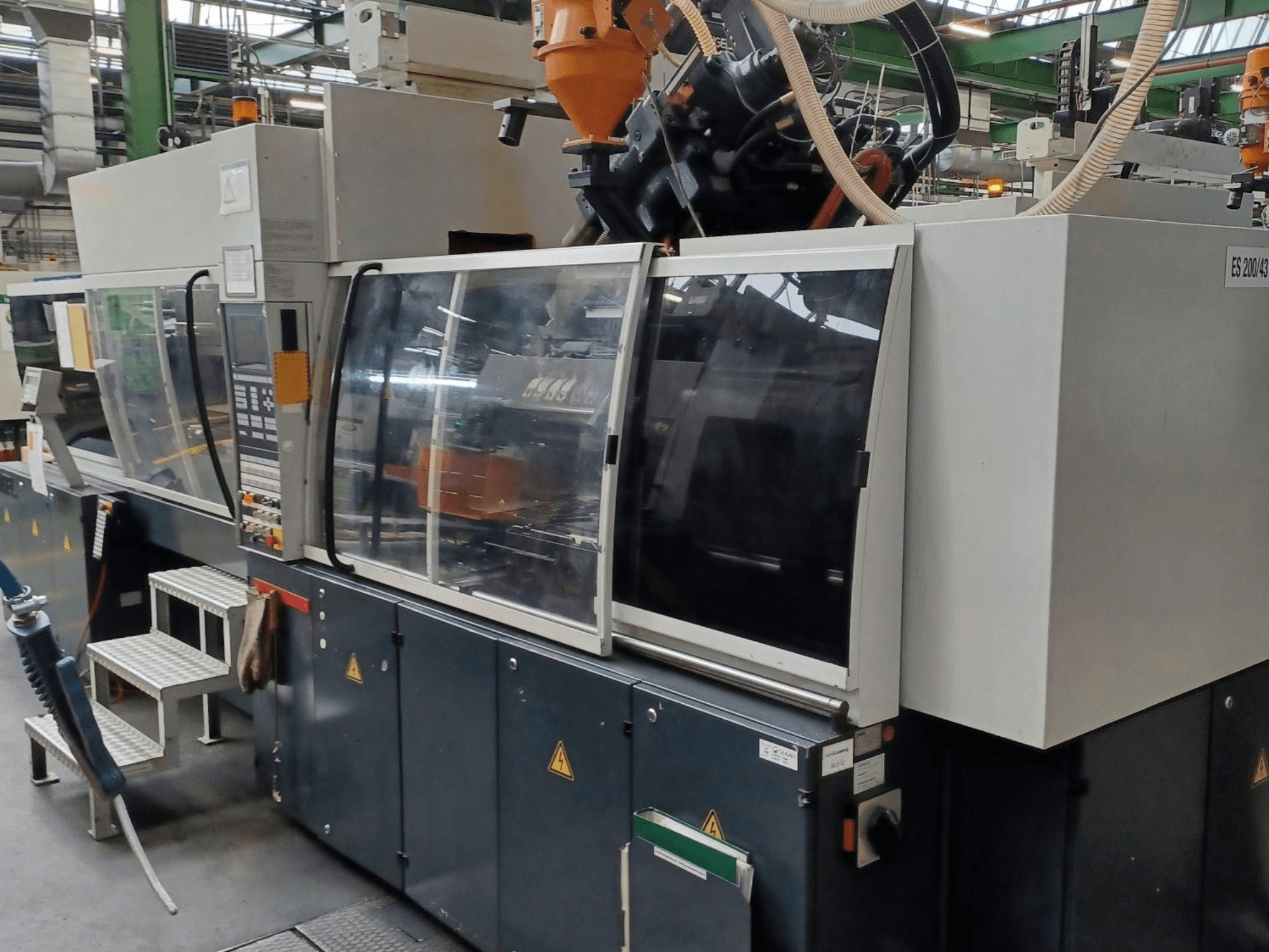 Front view of a plastic injection molding machine, brand and model unknown, featuring transparent safety doors and control panel.